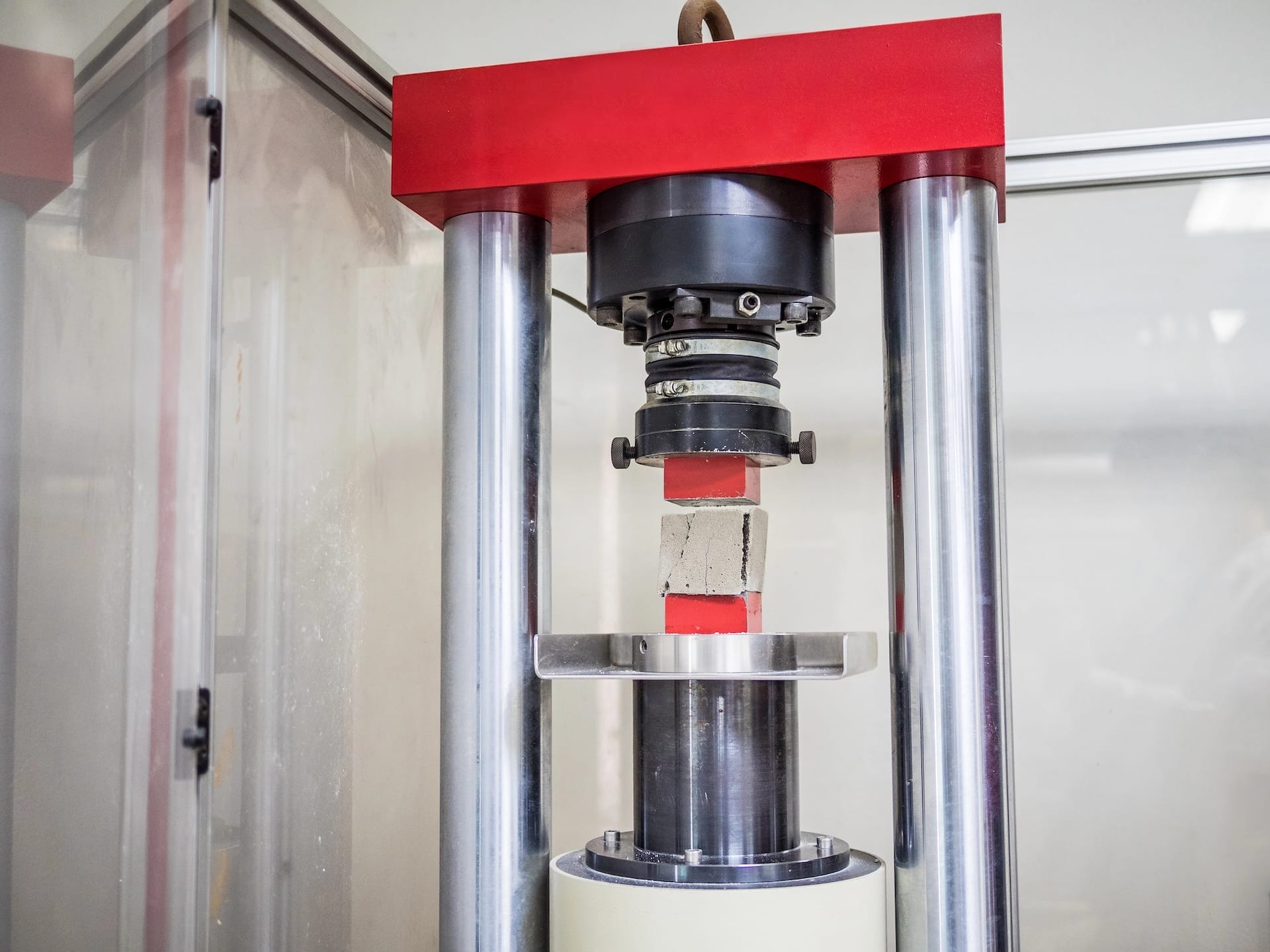 A hydraulic press machine applying force to crush a concrete block specimen between two plates during a compression test.